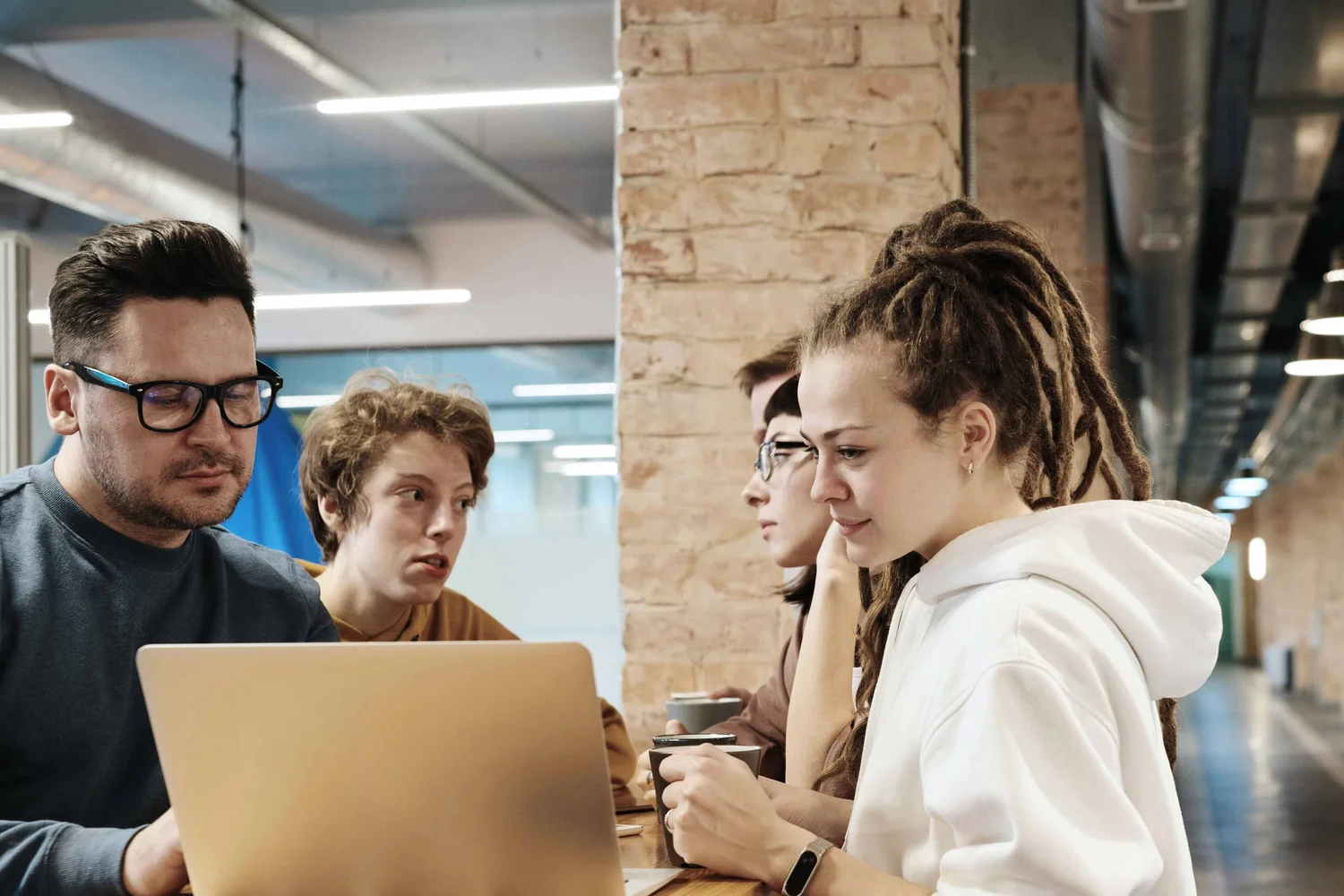 Five people gathered around a laptop in a modern office, mid-discussion.